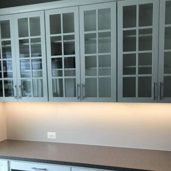 Modern kitchen with gray glass-front cabinets and a brown countertop along a lit backsplash.