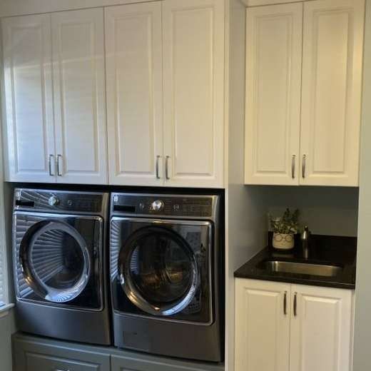 Laundry room with white cabinets above front-loading washer and dryer, plus a small countertop nook with plants