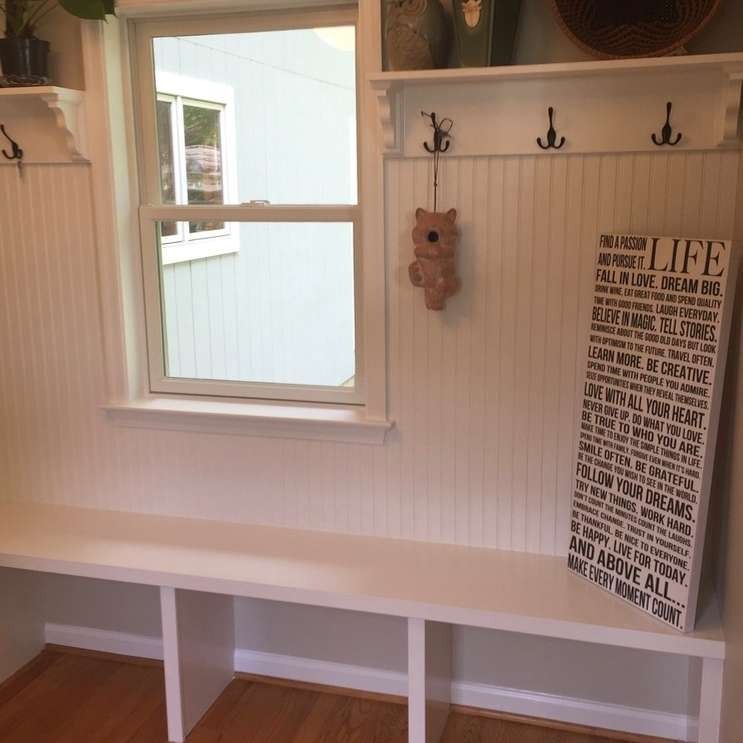 White built-in bench under a window with hooks, teddy bear, and framed “LIFE” print in a light room