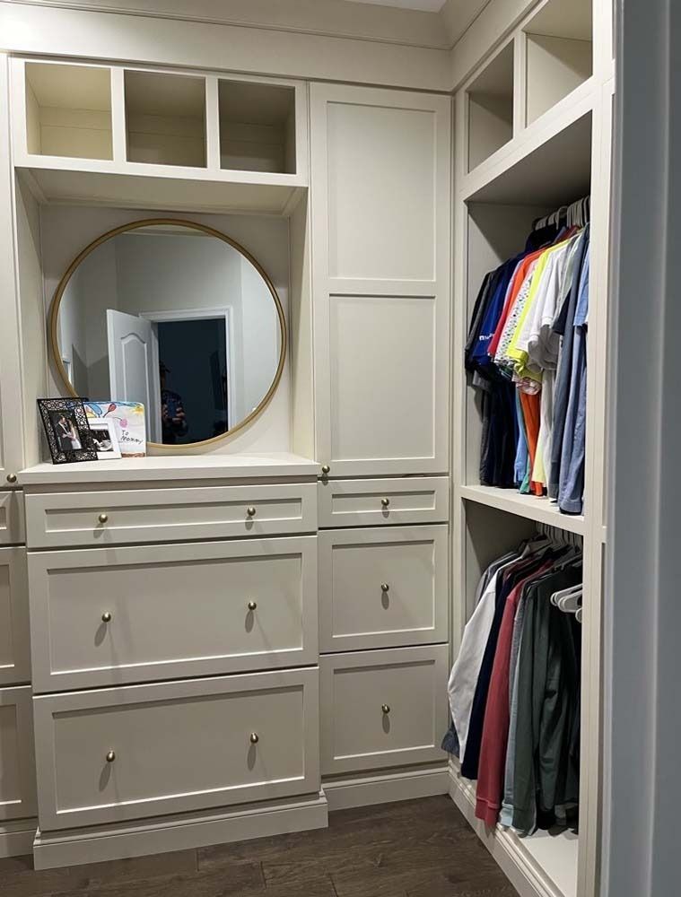 Built-in closet with drawers, open shelves, and hanging clothes beside a large round mirror.