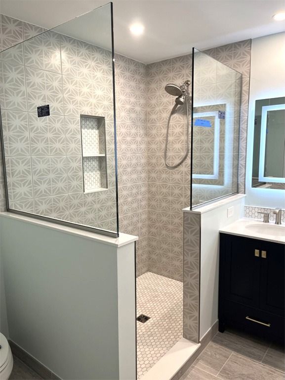 Modern bathroom shower with glass partition, patterned tile, and white vanity under a window
