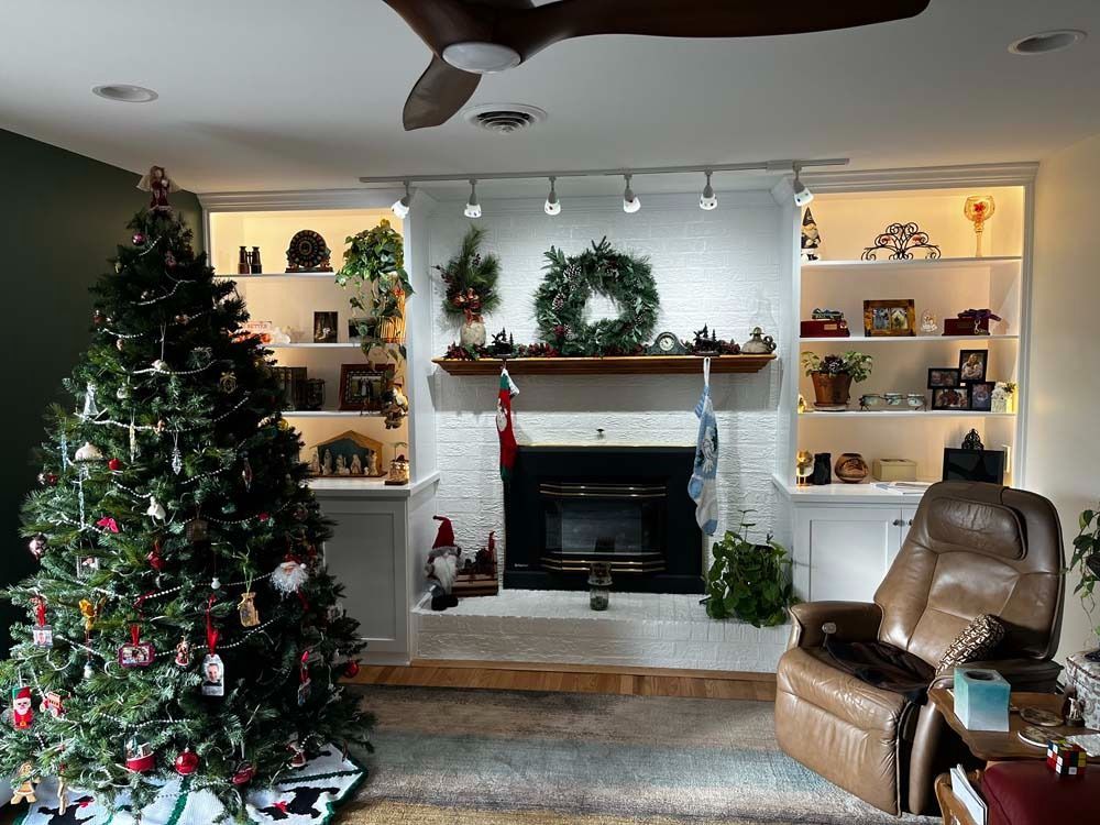 Christmas-decorated living room with fireplace, tree, shelves, and leather recliner