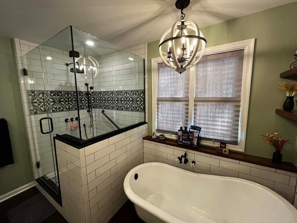 Modern bathroom with glass shower, white freestanding tub, and pendant light by window