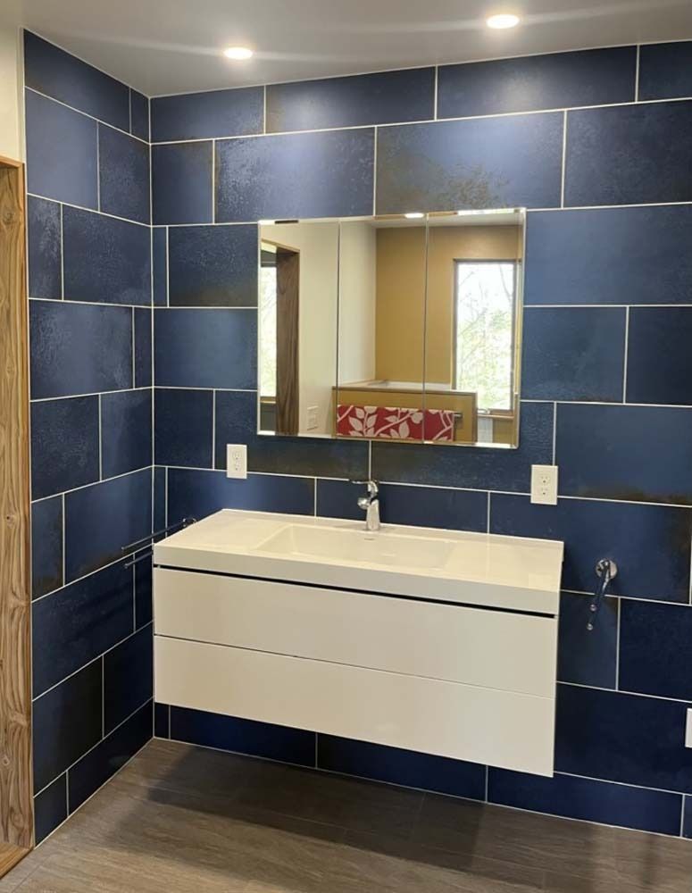 Modern bathroom with blue tile walls, floating white vanity, and rectangular mirror above sink