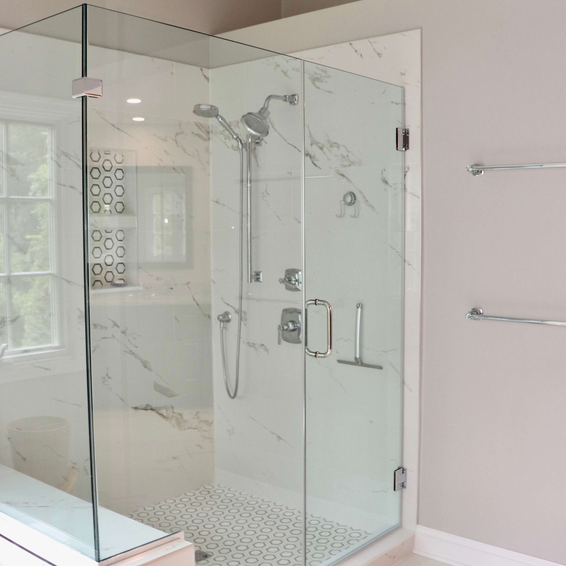 Glass walk-in shower with chrome fixtures and pebble tile floor in a bright bathroom