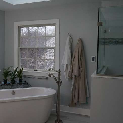 Modern bathroom with a freestanding tub, window, glass shower, and robes hanging on the wall