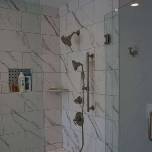 Modern tiled shower with glass door, marble-look walls, built-in niche, and chrome shower fixtures