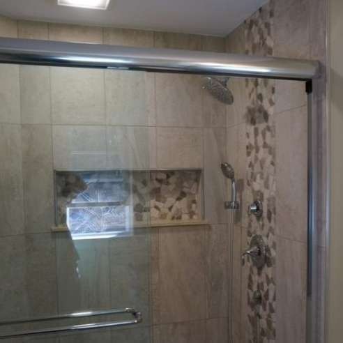 Glass shower enclosure with beige tile and mosaic accent wall in a bathroom
