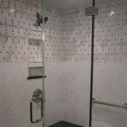 Empty tiled shower with glass door, chrome grab bar, soap shelf, and handheld showerhead.
