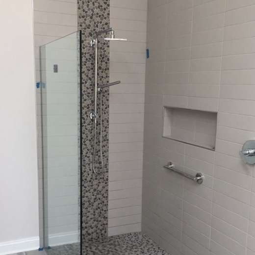 Modern shower with glass door, mosaic tile column, built-in shelf, and chrome grab bar on white tile wall