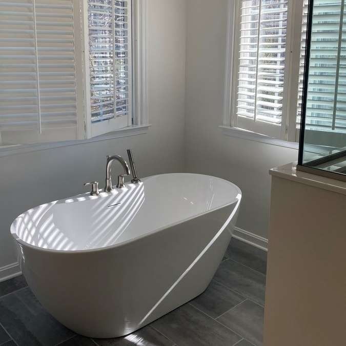 Modern white freestanding bathtub in a bright bathroom with gray tile and white blinds
