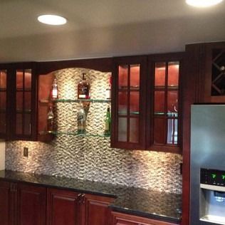 Modern kitchen with dark wood cabinets, mosaic backsplash, black countertop, and stainless refrigerator