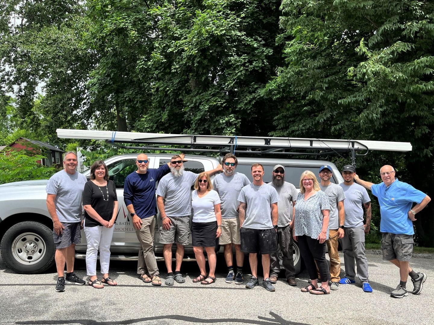Group of rowers standing with an oarboat on a road, posing in front of trees and a truck