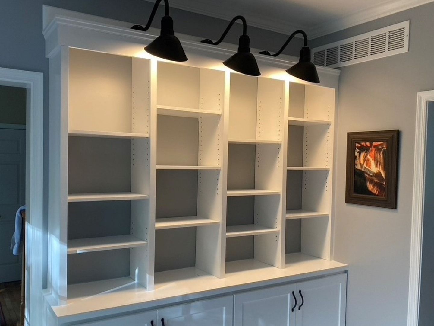 White built-in shelving with spotlights above a cabinet in a gray room