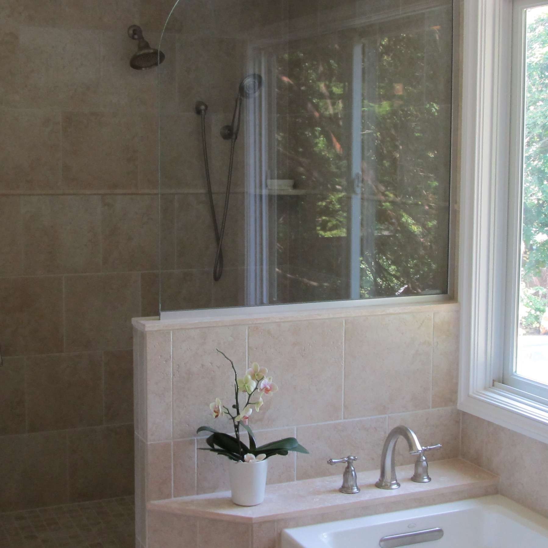 Modern bathroom with tiled shower, window, and a sink holding a small potted orchid