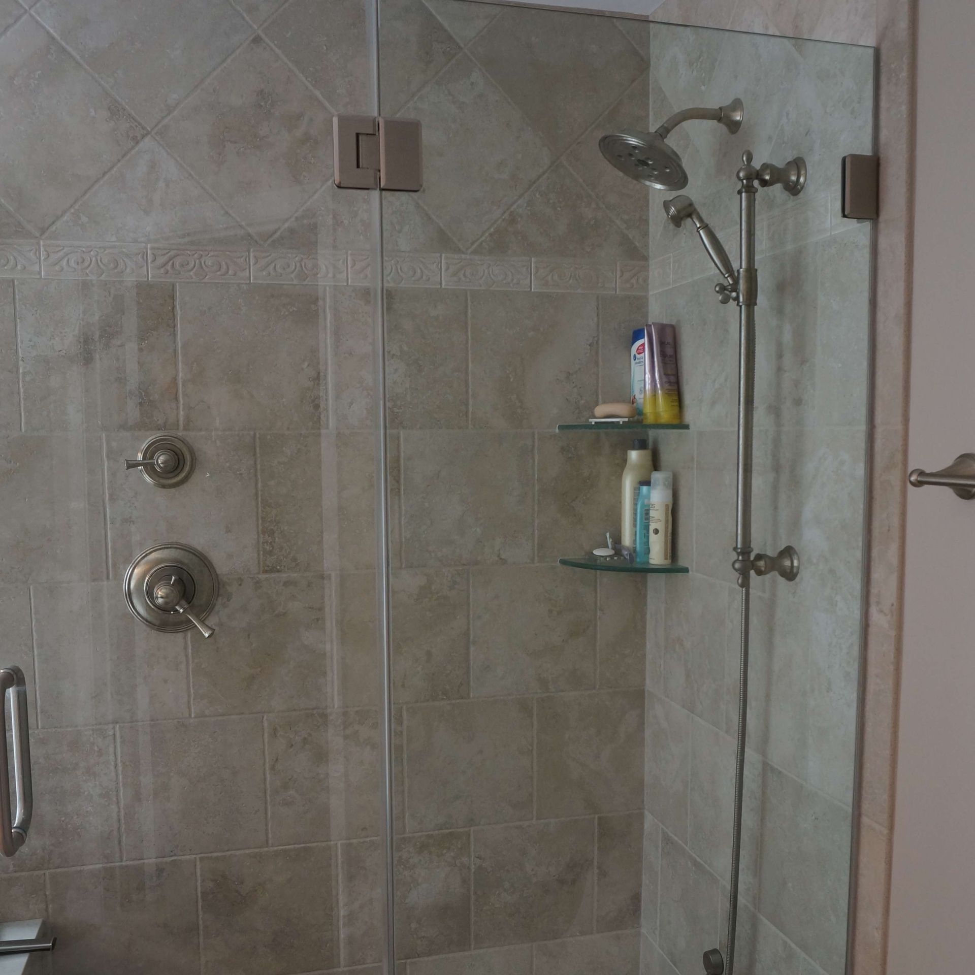 Glass shower stall with beige tile walls and built-in corner shelves holding toiletries.