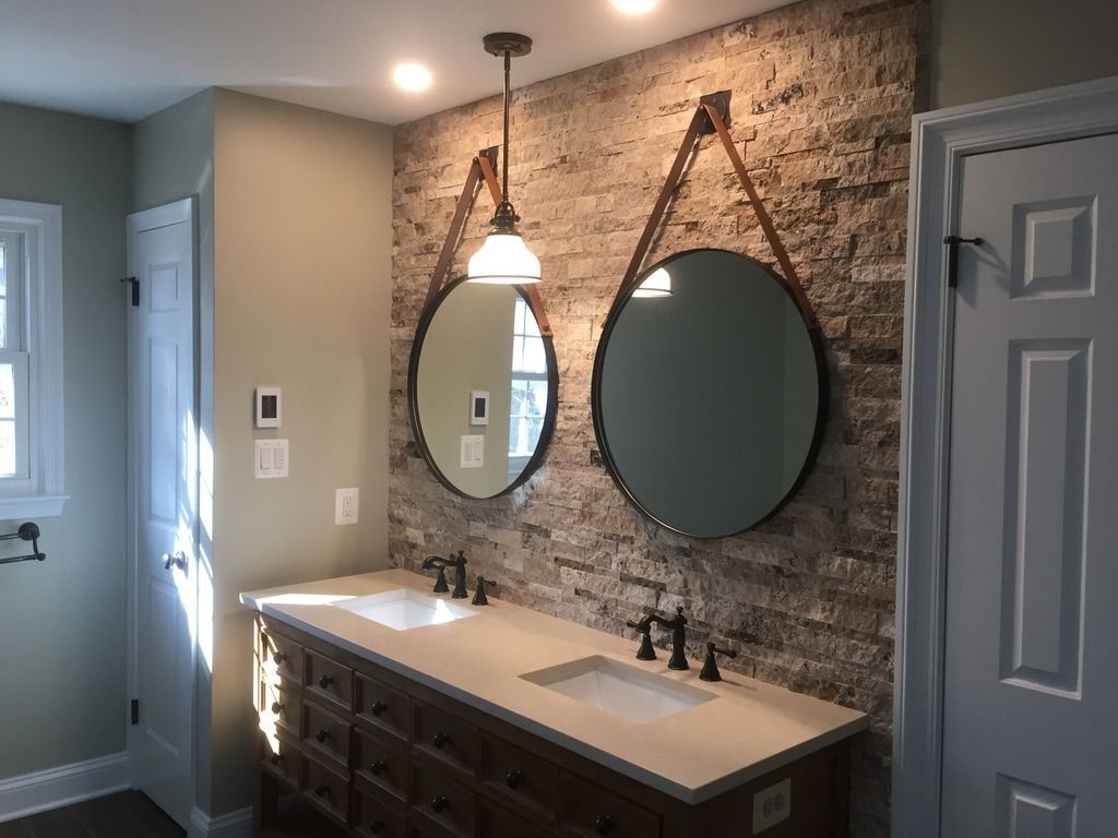 Bathroom with double vanity, round mirrors, pendant light, and stone accent wall