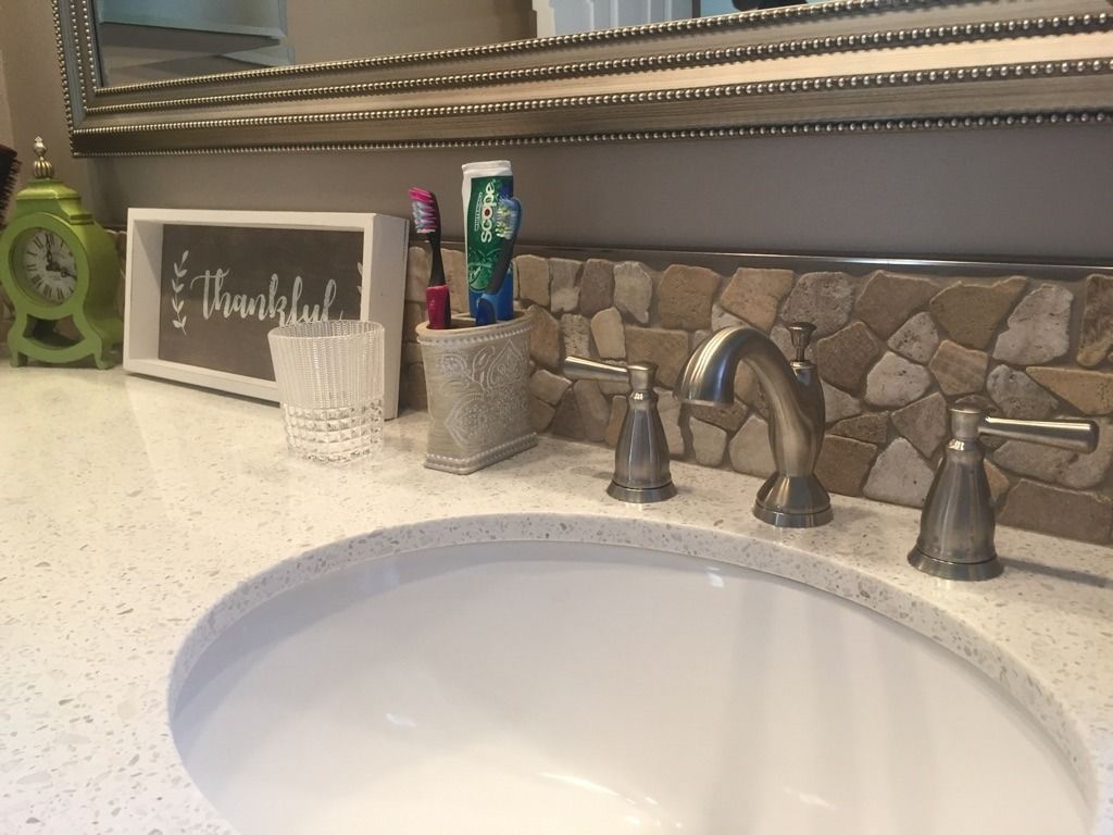 Bathroom sink with chrome faucet, stone backsplash, and countertop decor including a chalkboard sign.