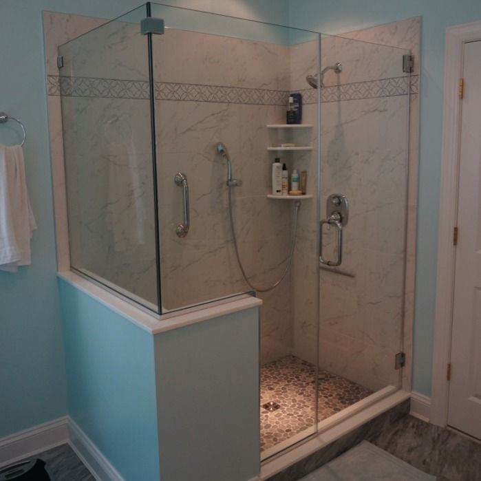 Glass walk-in shower with beige tile, built-in shelves, and a pebble shower floor in a bathroom
