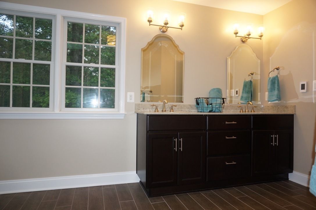 Bathroom vanity with dark cabinets, large mirror, wall sconces, and a window on the left.