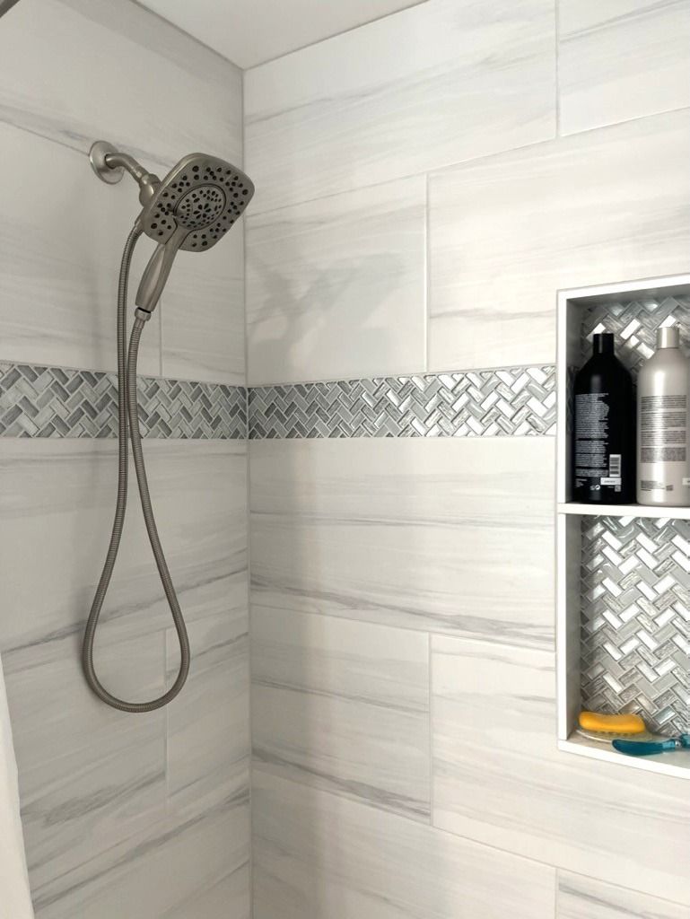 Modern tiled shower with handheld showerhead and built-in shelf of toiletries