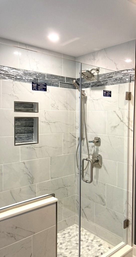 Modern glass shower with white tiled walls, chrome fixtures, and mosaic border in a bathroom