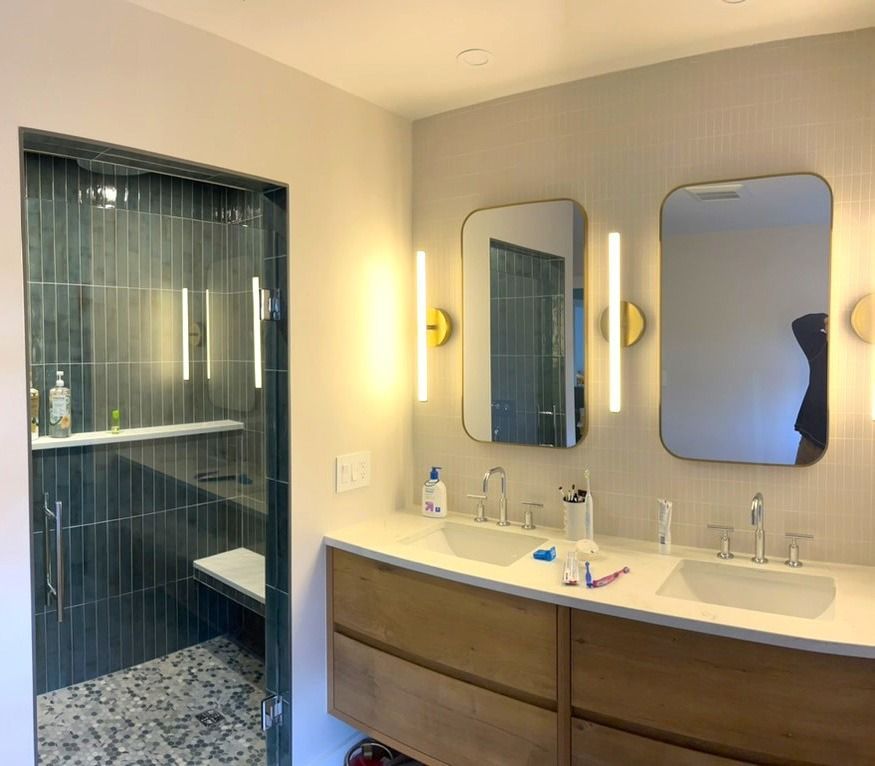 Modern bathroom with double sink vanity, mirrors, and a glass-enclosed shower with tiled walls