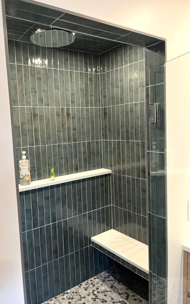 Small tiled shower stall with dark gray walls, white bench, and round overhead showerhead