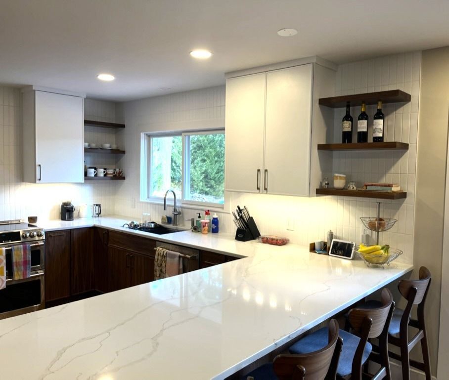 Bright modern kitchen with white counters, dark cabinets, window, and bar stools at a peninsula