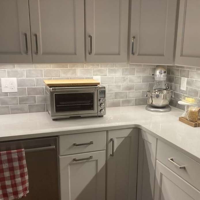Modern kitchen counter with gray tile backsplash, toaster oven, stand mixer, and white cabinets