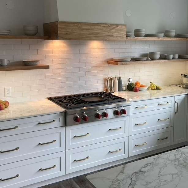 Bright modern kitchen with white cabinets, gas range, wood shelves, and marble countertops