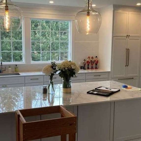Bright modern kitchen with white cabinets, marble island, pendant lights, flowers, and a window garden view