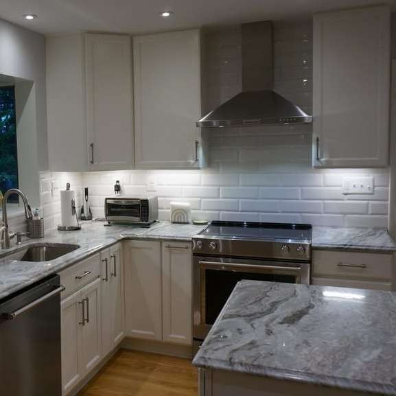 Modern white kitchen with gray marble island, stainless steel appliances, and subway tile backsplash