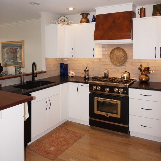 Modern white kitchen with black countertops, black stove, and copper range hood