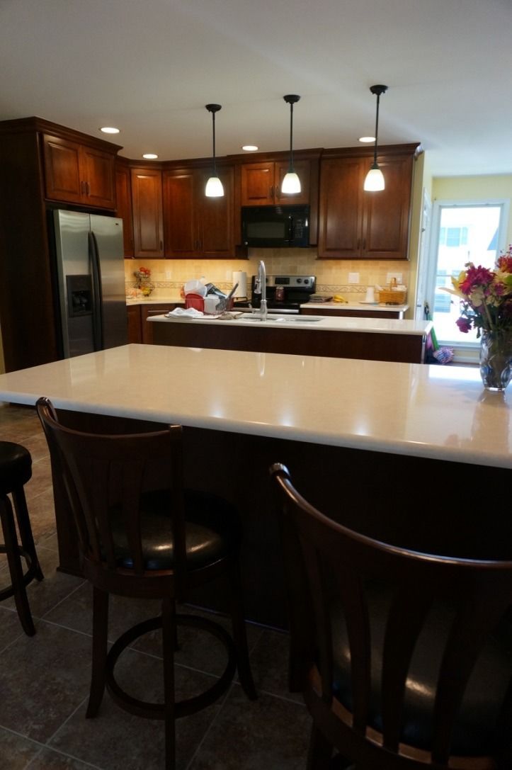 Kitchen with white island, dark wood cabinets, pendant lights, and bar stools