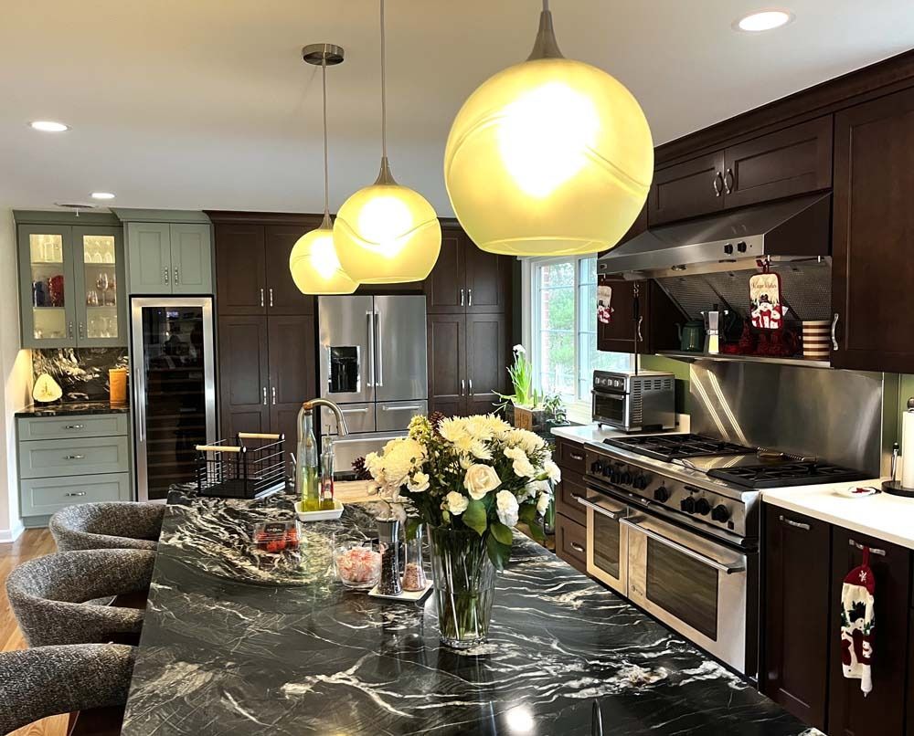 Modern kitchen with dark cabinets, marble island, pendant lights, stainless appliances, and a flower centerpiece