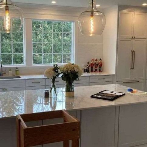 Bright white kitchen with large windows, marble island, pendant lights, and flowers on the counter.