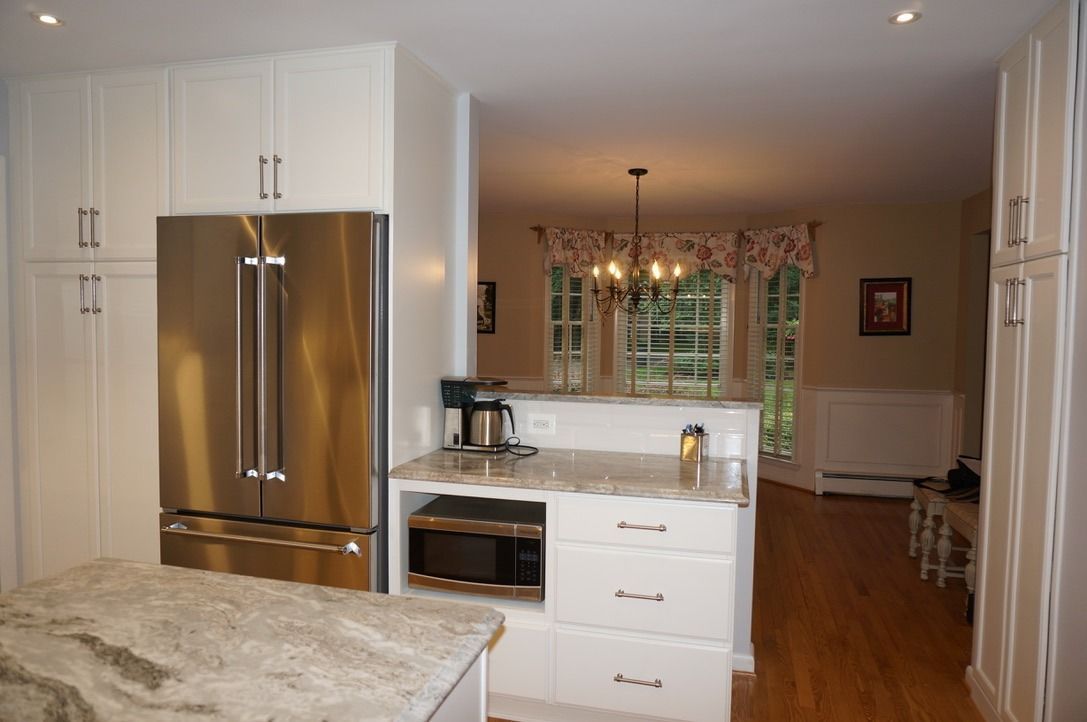 Bright kitchen with stainless steel fridge, white cabinets, and a view into a dining area with hardwood floors.