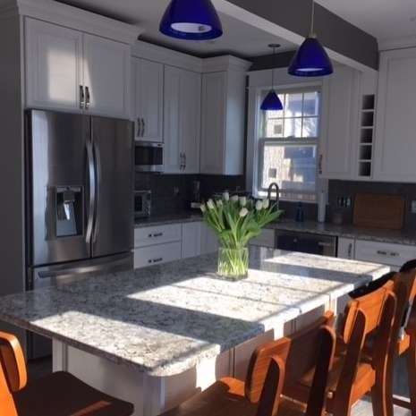 Modern kitchen with granite island, stainless steel appliances, blue pendant lights, and a vase of tulips.