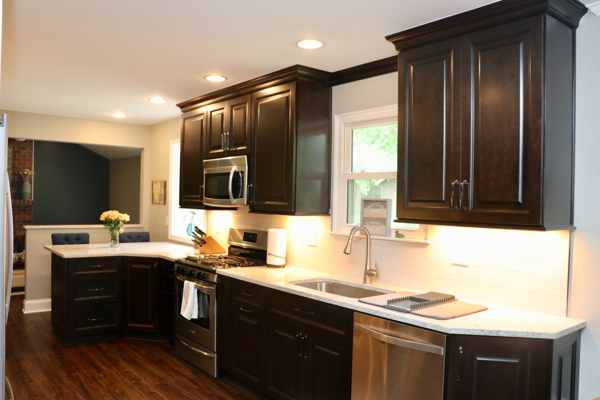 Modern kitchen with dark wood cabinets, white countertops, stainless appliances, and a window over the sink