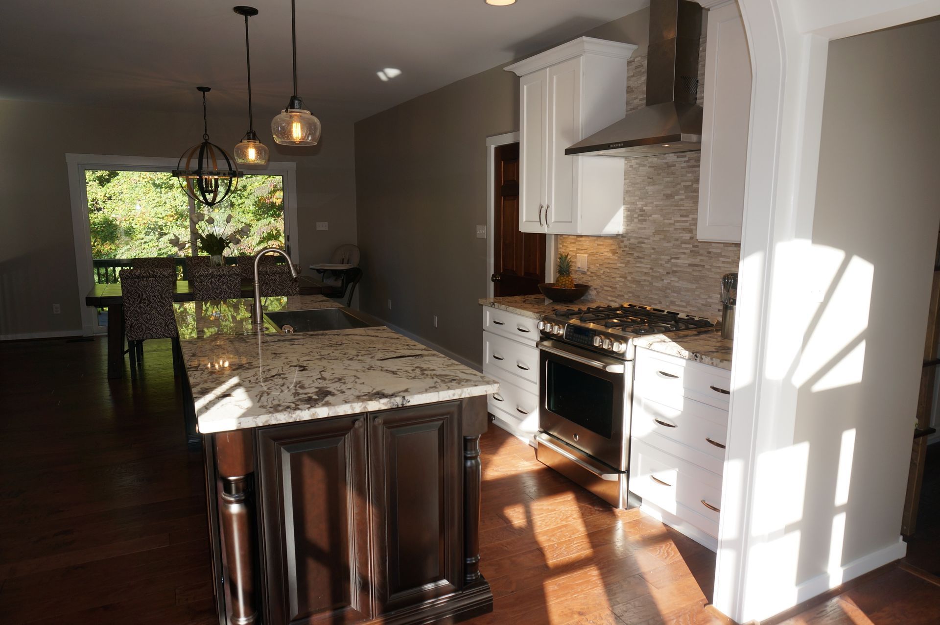 Bright kitchen with granite island, white cabinets, pendant lights, and sunlight on hardwood floors.