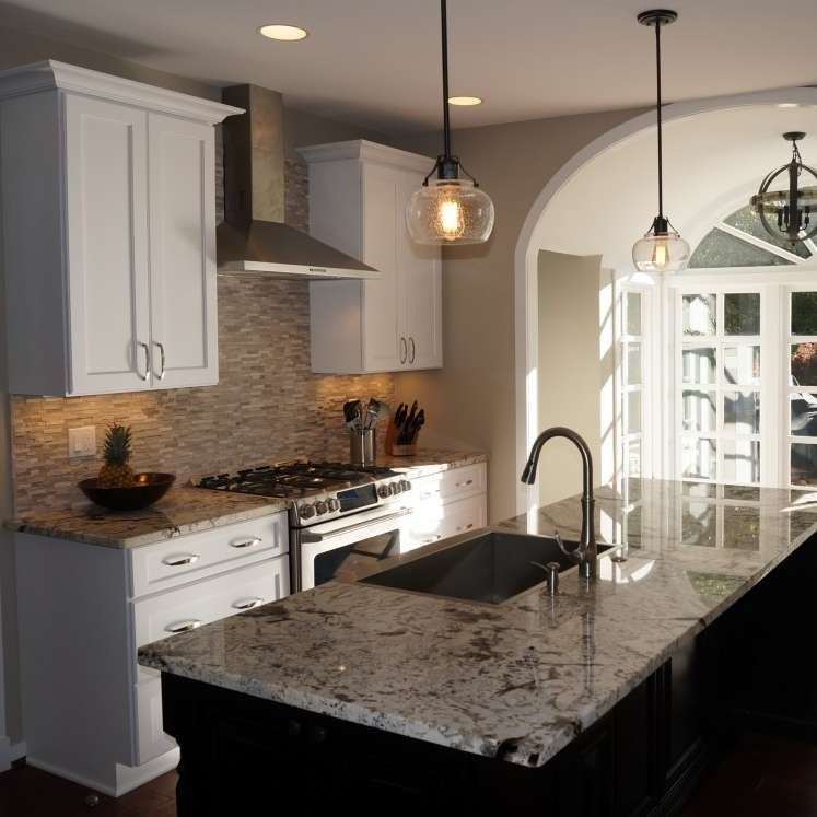 Modern kitchen with white cabinets, granite island, stainless appliances, and arched doorway to a bright dining area