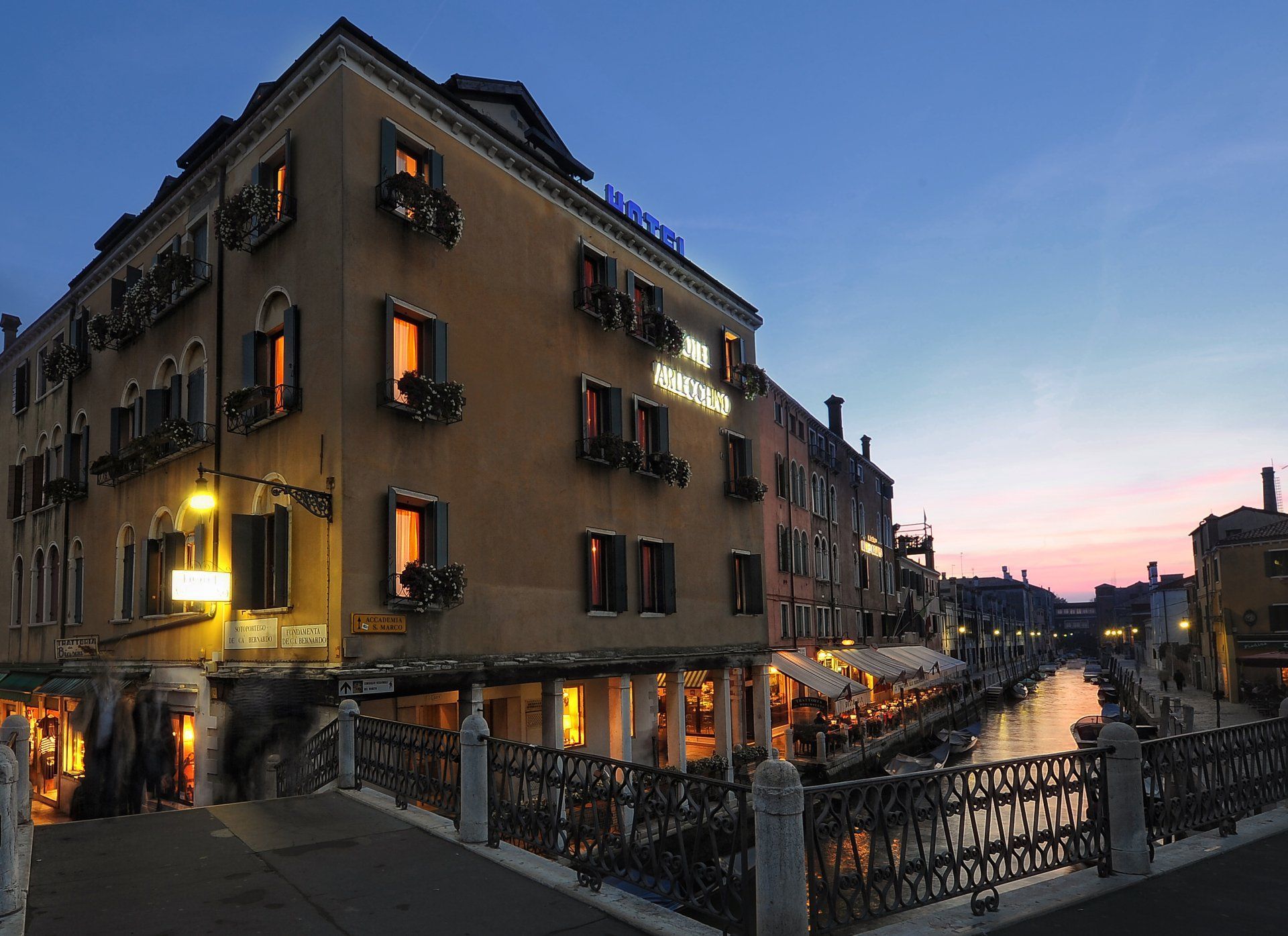Edificio lungo il canale al crepuscolo, con finestre illuminate da una luce calda e riflessi sull’acqua