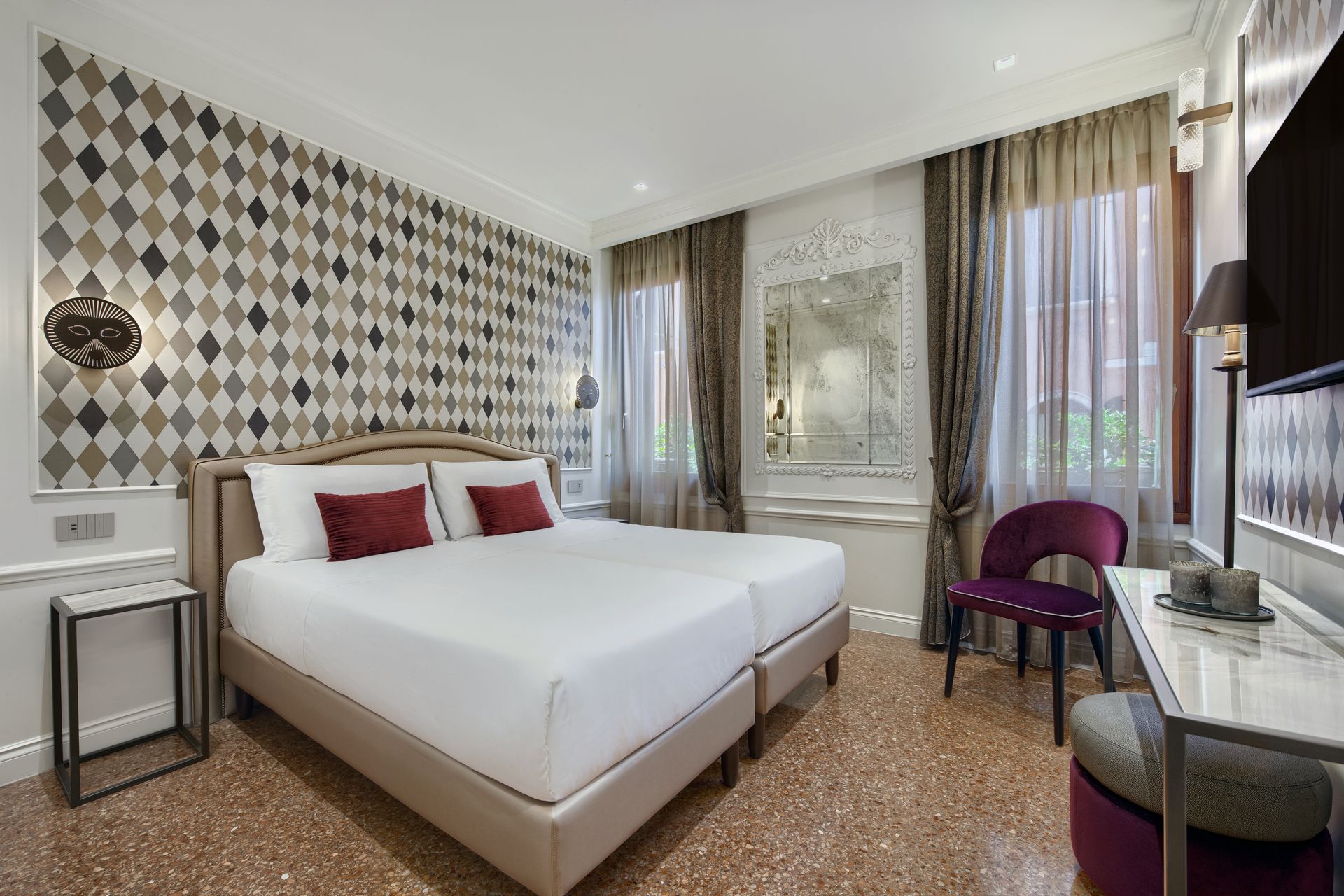 Camera d’albergo moderna con un letto bianco, una parete decorata, tende alla finestra e una sedia accanto alla finestra