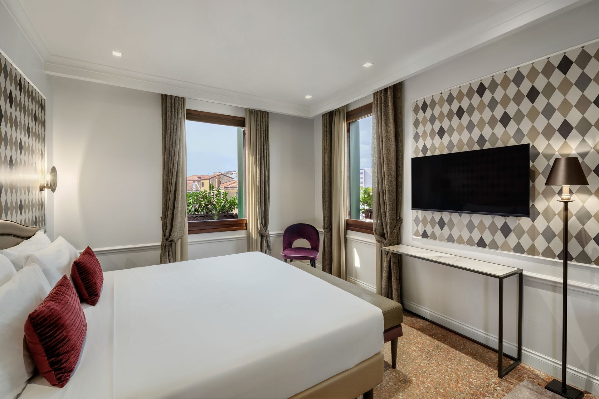 Modern hotel bedroom with white bed, TV, window view, and patterned accent wall