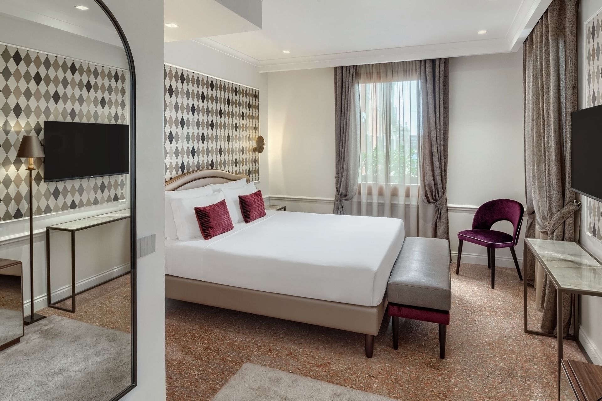 Modern hotel room with a king bed, wall-mounted TV, desk, chair, and window with curtains