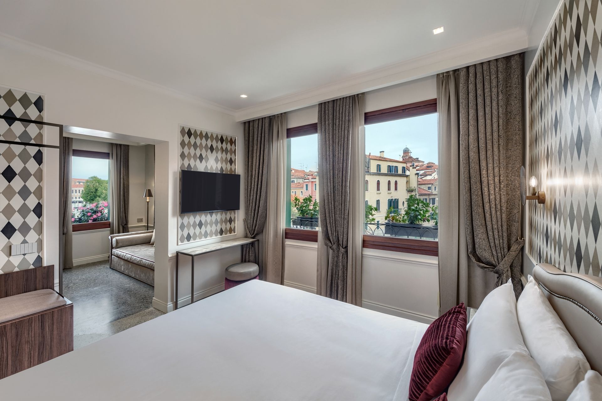 Modern hotel bedroom with large windows, white bed, desk, and city view