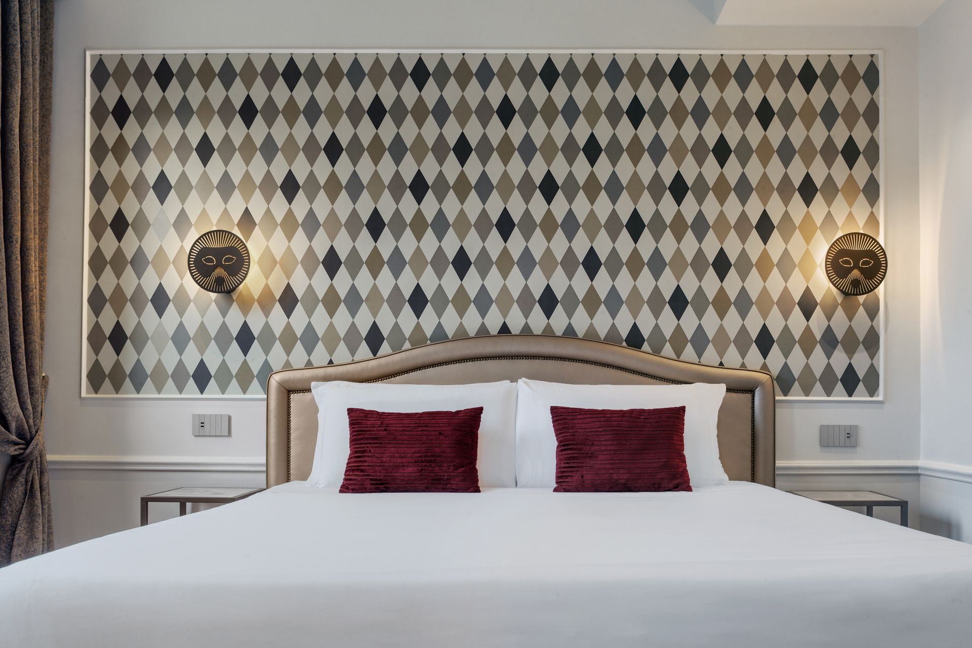 Hotel bedroom with large bed, white linens, red pillows, and patterned wall panels with sconces