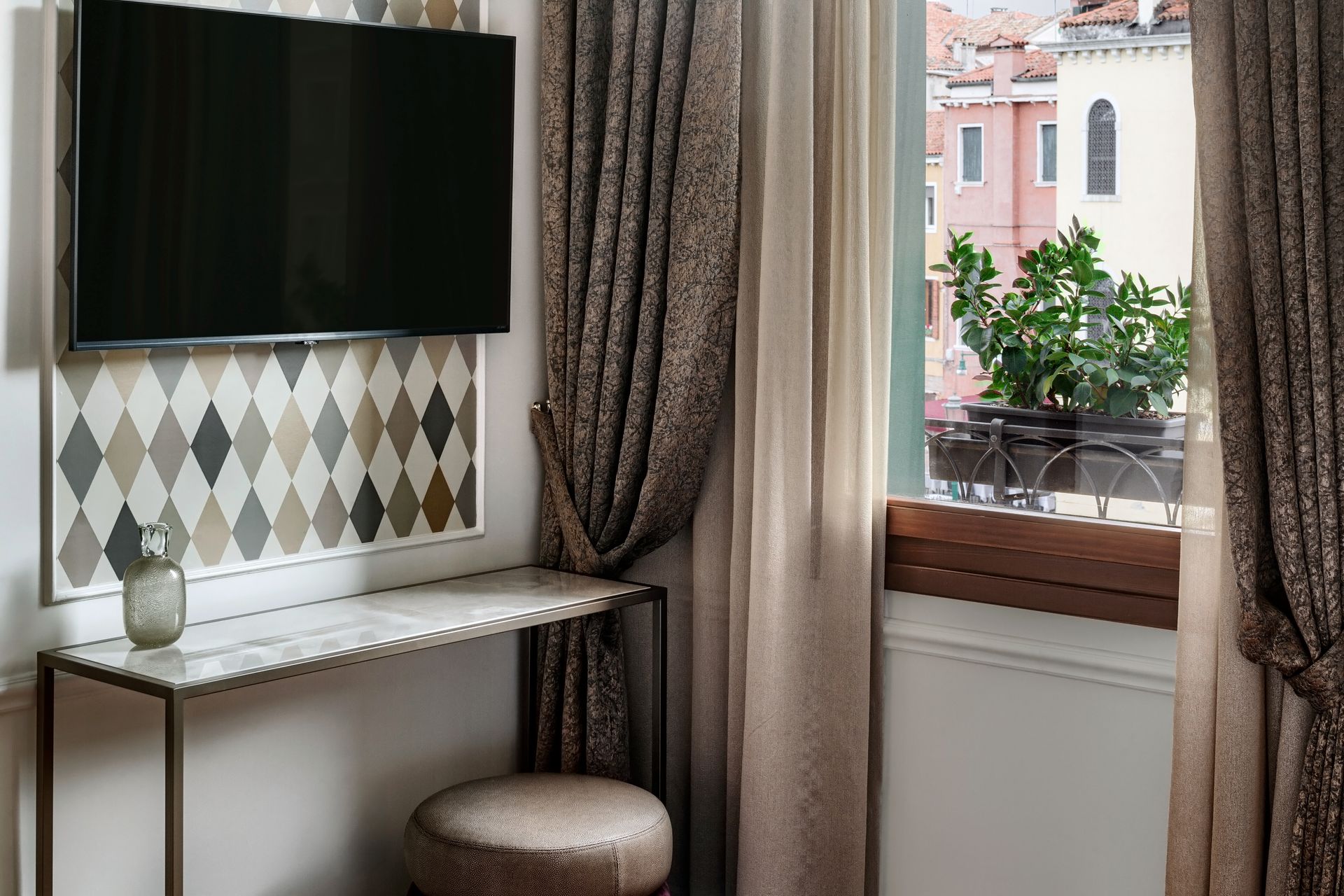 Cozy room corner with vanity table, wall mirror, stool, and window with curtains overlooking a building