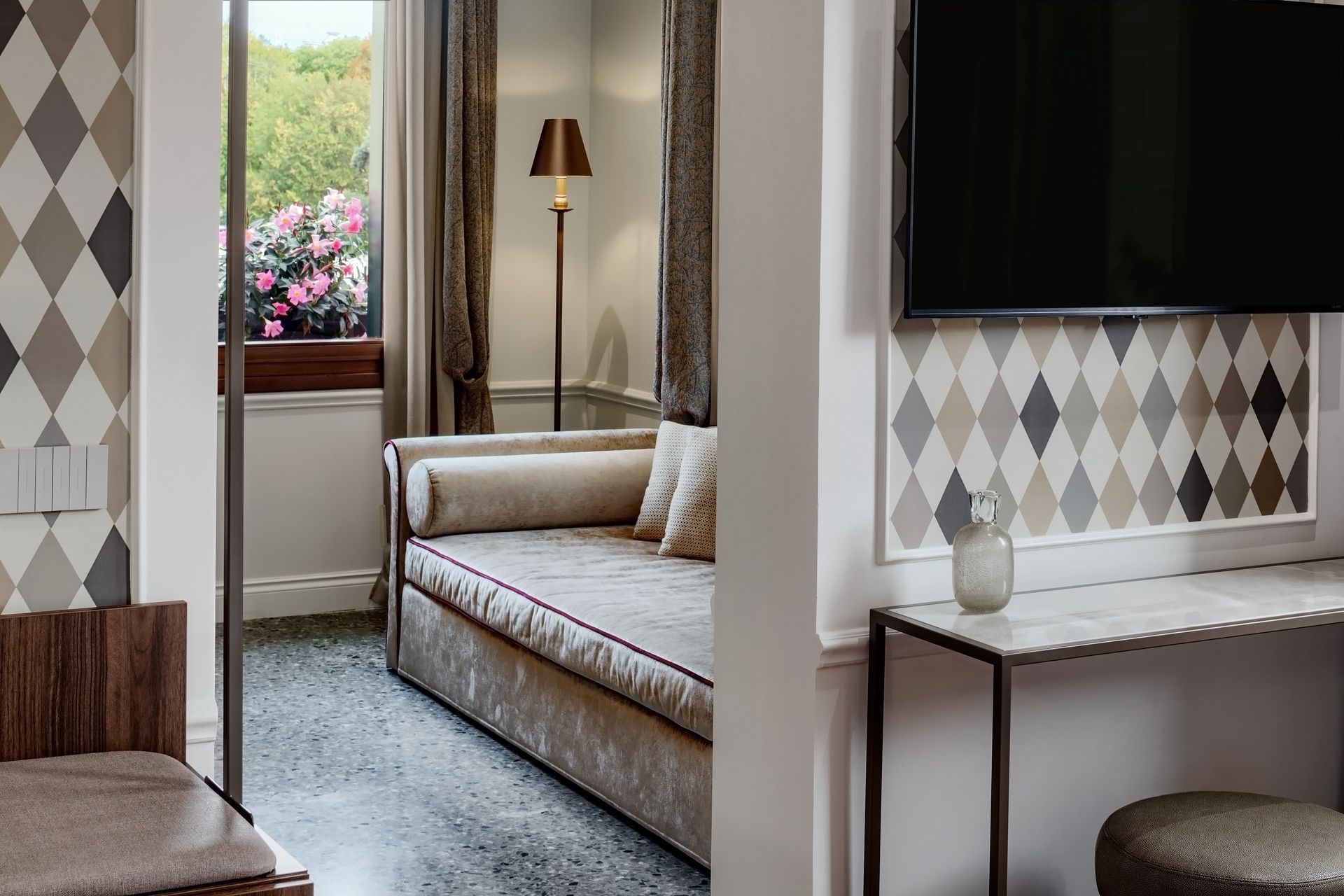 Modern living room with a sofa, floor lamp, patterned wallpaper, and window seat overlooking flowers